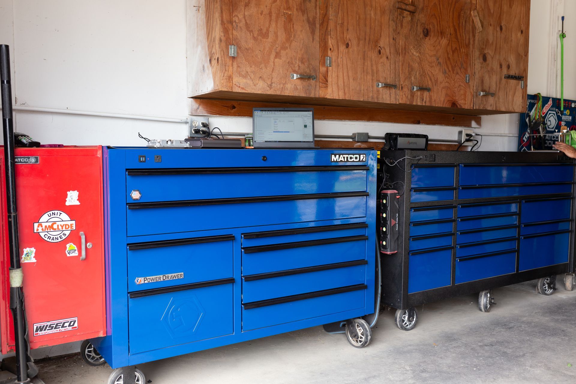 A blue tool chest next to a red toolbox, against a white wall with wooden cabinets above.