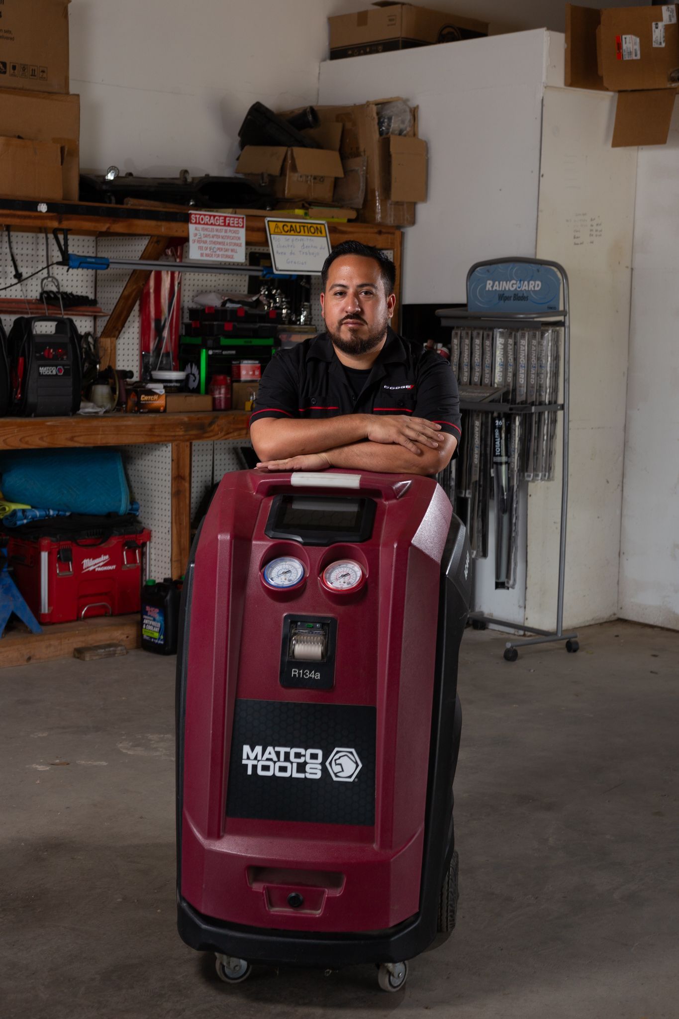 Man leaning on an automotive air conditioning service machine in a garage.