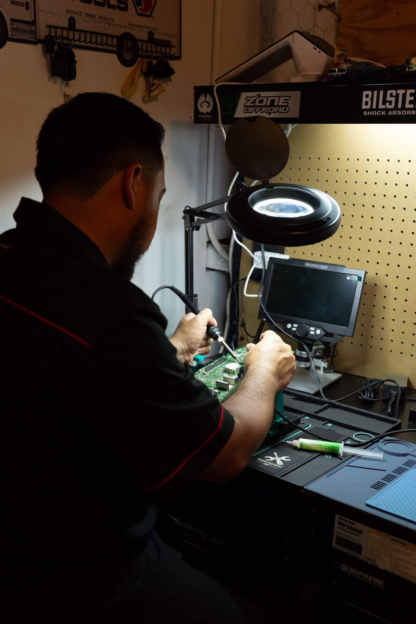 A person soldering circuit board at a workbench, using a magnifying lamp.