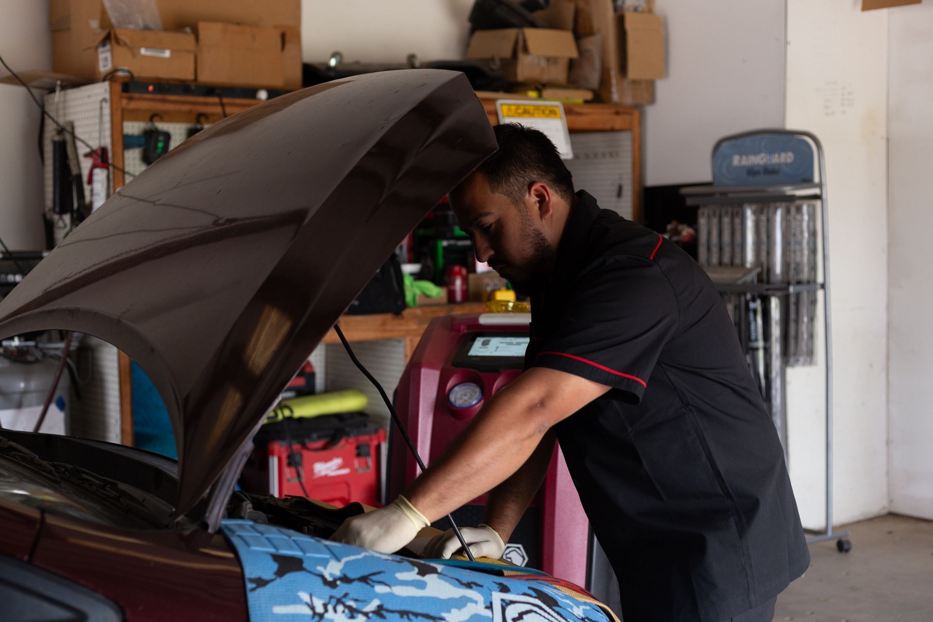 Mechanic working on a car with the hood up, using a machine in a garage.
