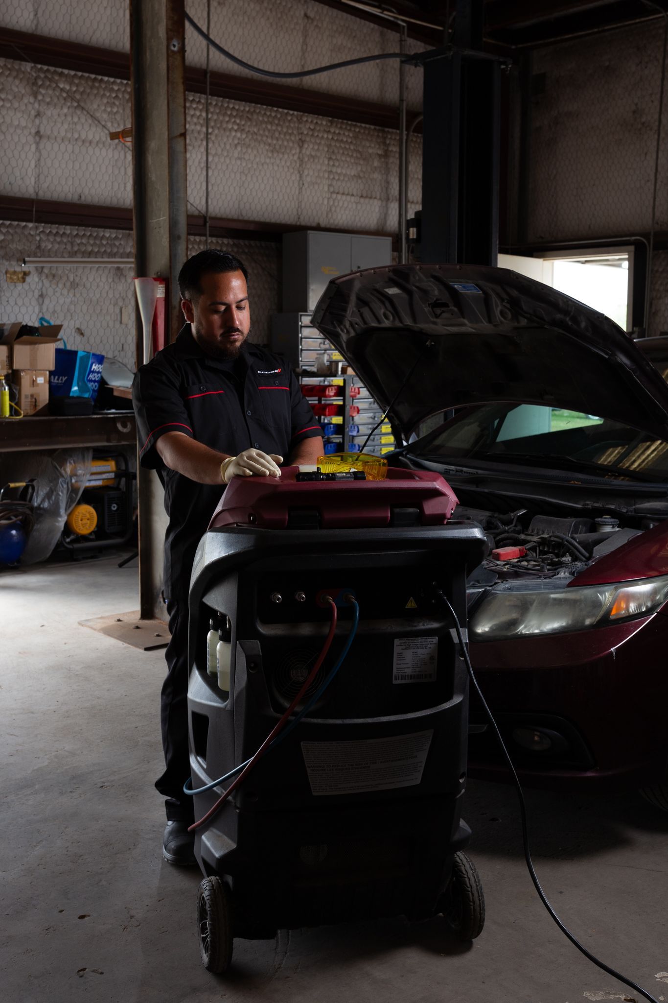 Mechanic using a machine to service a car's engine in an auto repair shop.