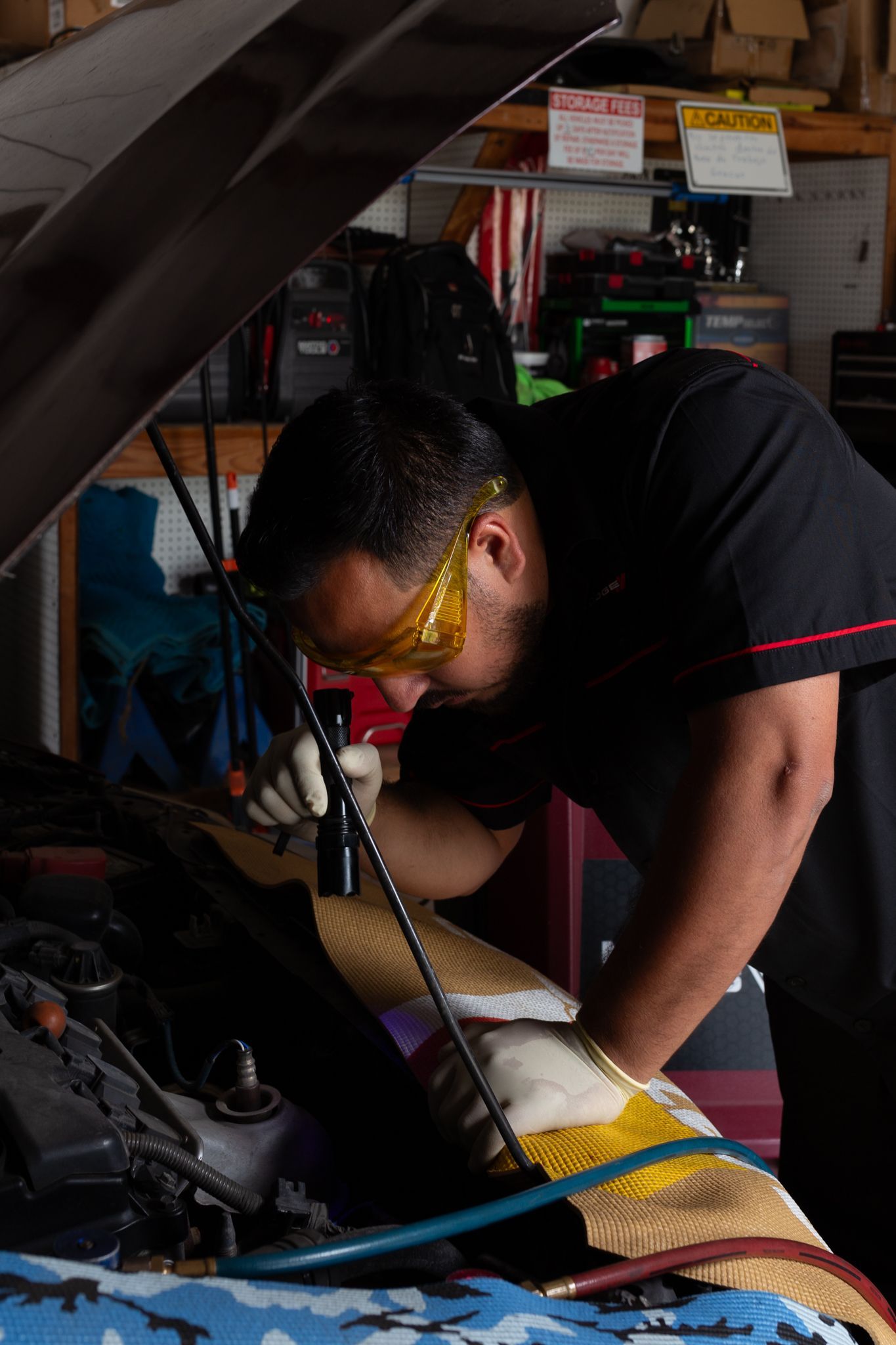 Mechanic in safety glasses working on a car engine in a garage.