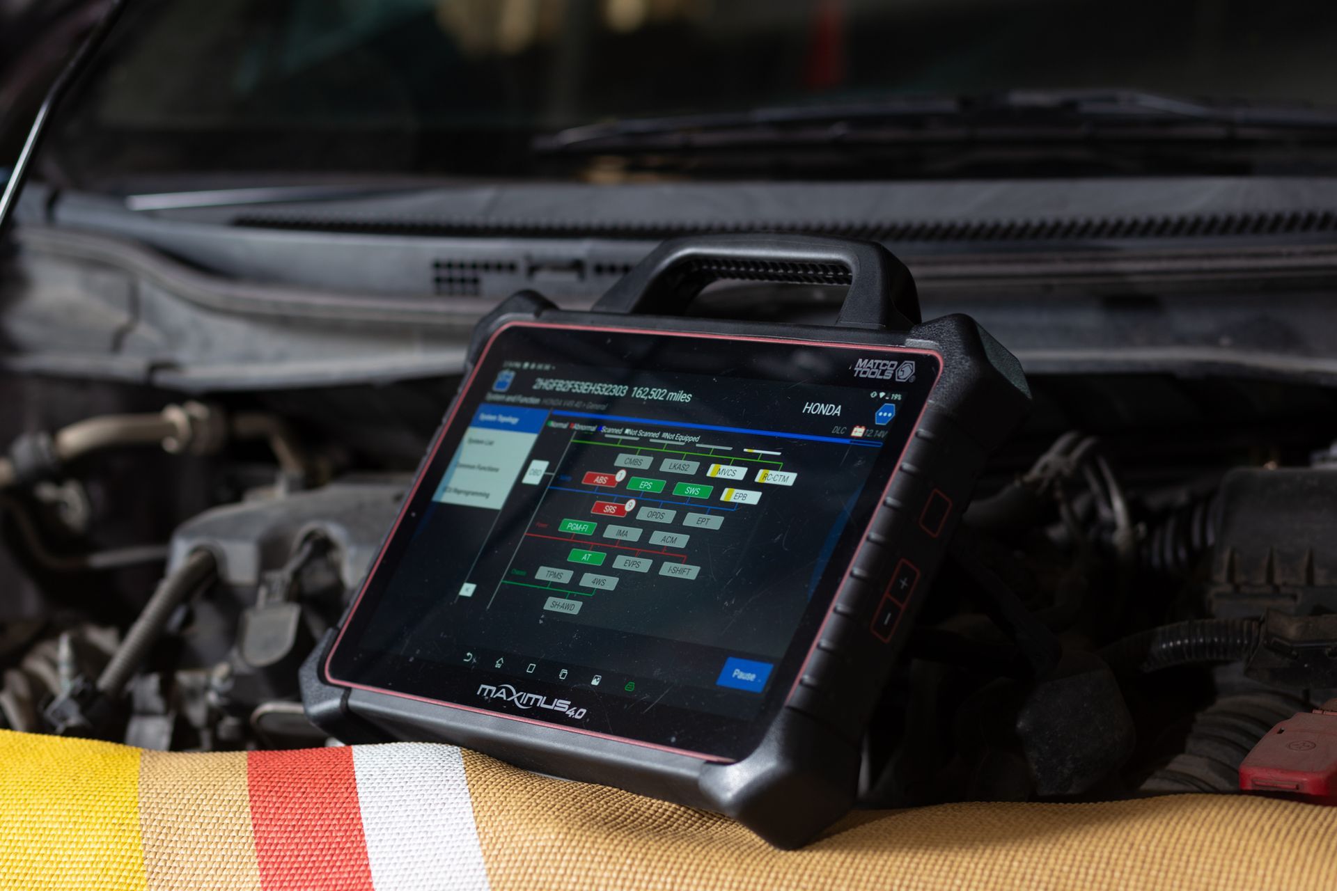 Tablet diagnostic tool displaying car engine data on an open car hood.