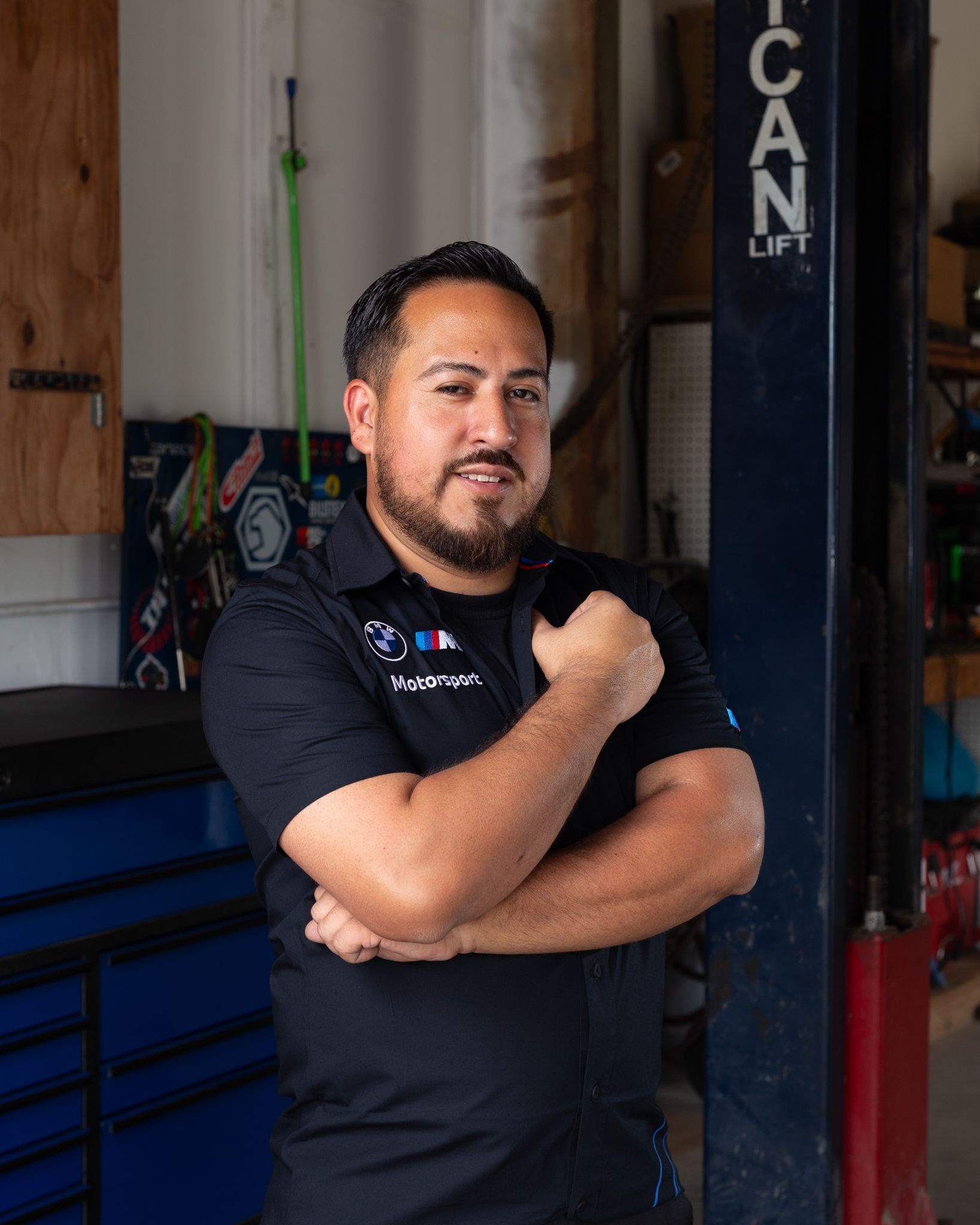 Man with crossed arms in a garage, wearing a black shirt. He is smiling.