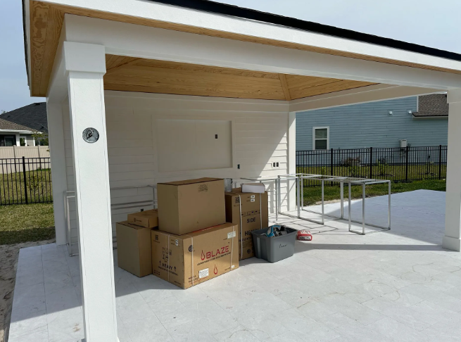 Covered patio with boxes and tables on a concrete surface, white columns and ceiling.