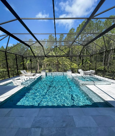 Swimming pool with screen enclosure; blue water, white stone patio, forest backdrop.
