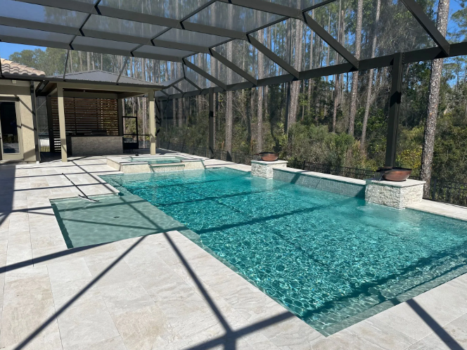 Swimming pool enclosed in a screened patio, adjacent to a wooded area. Light blue water, beige tiling.