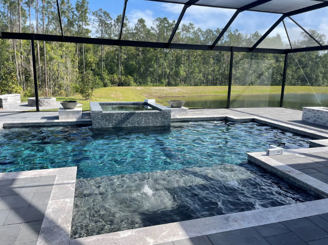 Outdoor swimming pool with a screen enclosure, surrounded by a patio and lush green background.