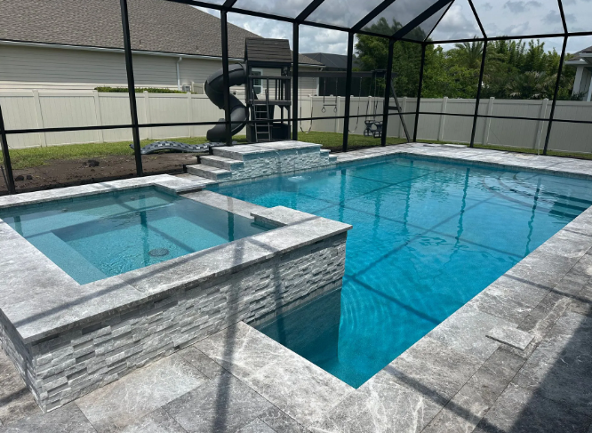 Pool with hot tub, slide, screened enclosure, and stone surround. Clear blue water.