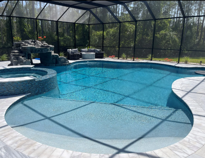 Swimming pool with waterfall, spa, surrounded by screen enclosure and tile patio; bright blue water.