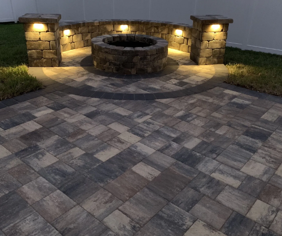 Brick patio with a built-in fire pit, stone wall with lights, and decorative paving stones.