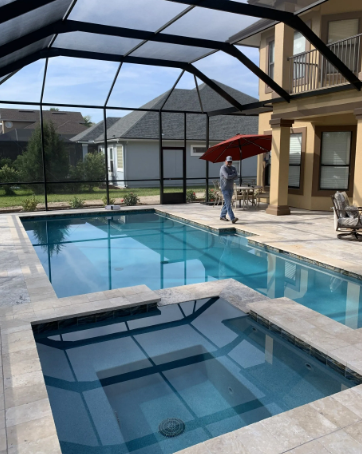 Pool and spa enclosed by a black screen structure. Man walks on the pool deck next to the pool, and a red umbrella is set up.