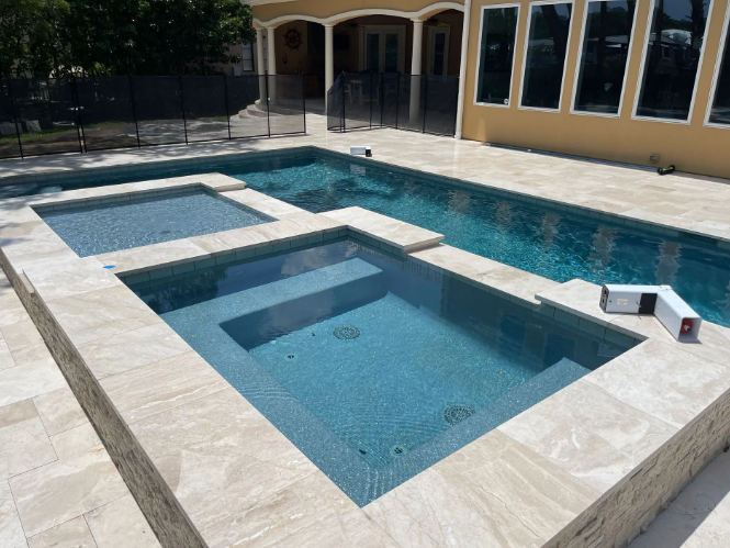 A multi-level swimming pool and spa area with a stone patio.