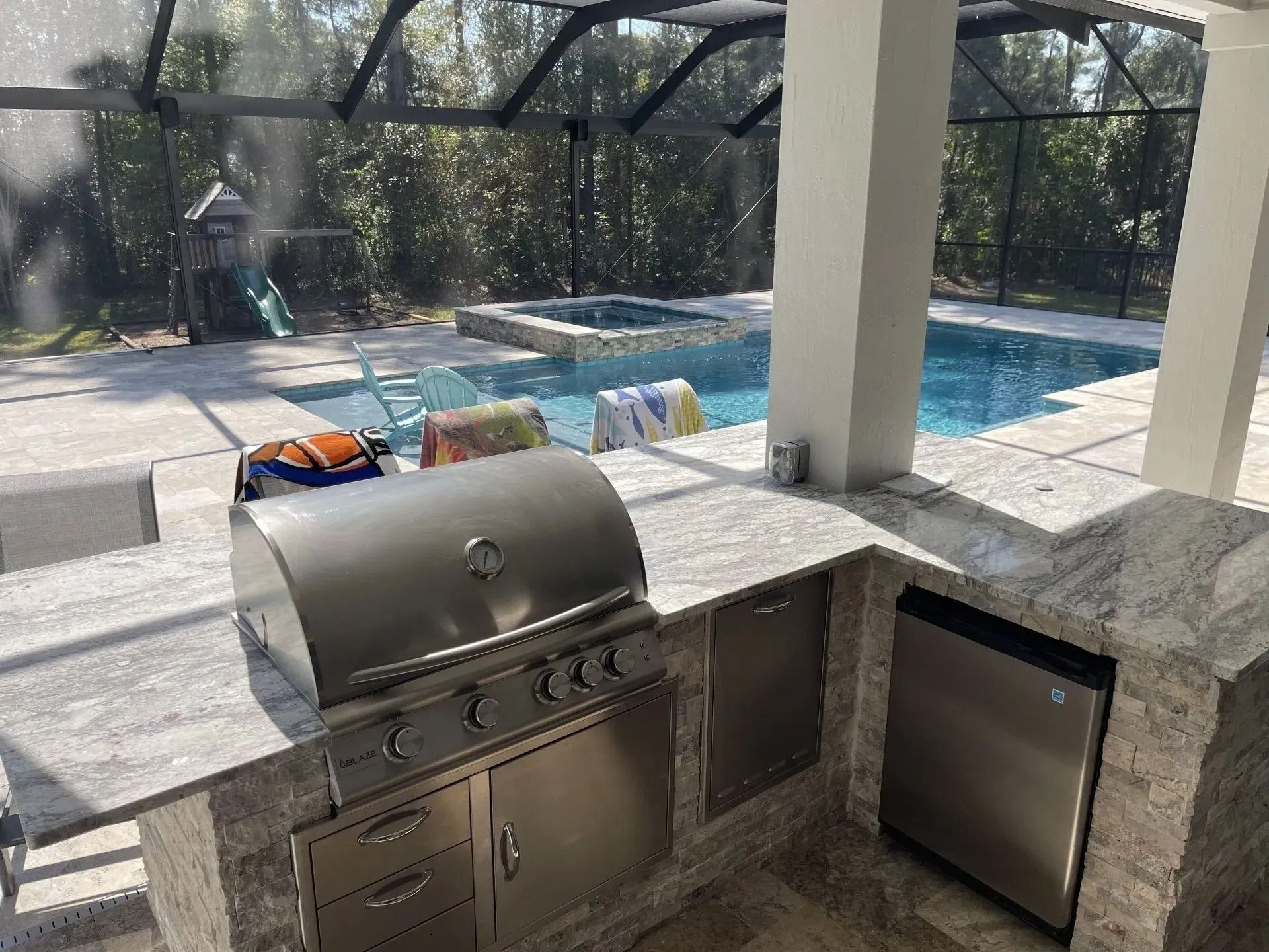 Outdoor kitchen with a grill, dishwasher, and pool in the background.