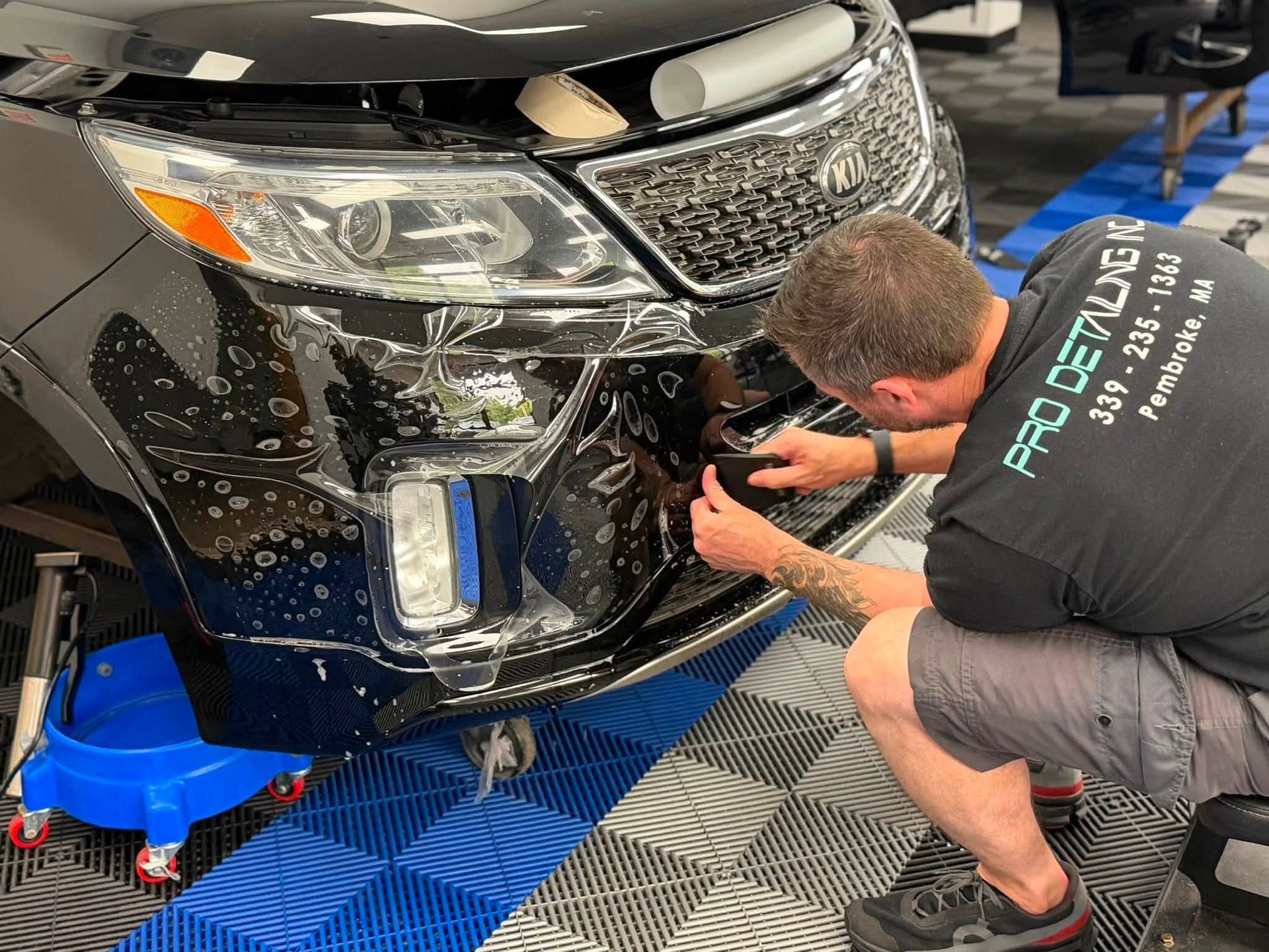 Mechanic repairing the front bumper of a black car on a blue lift in a workshop