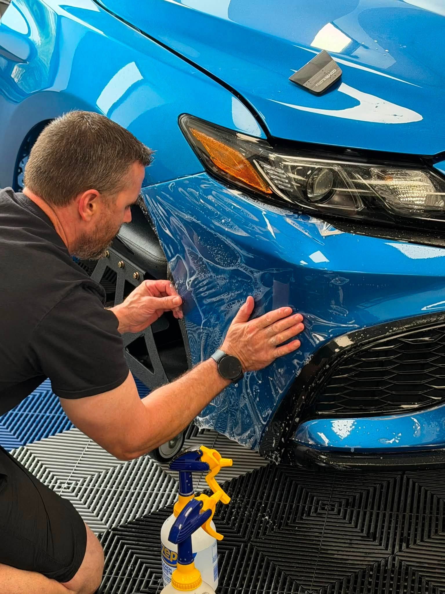 Mechanic inspecting the front bumper of a blue car in a workshop