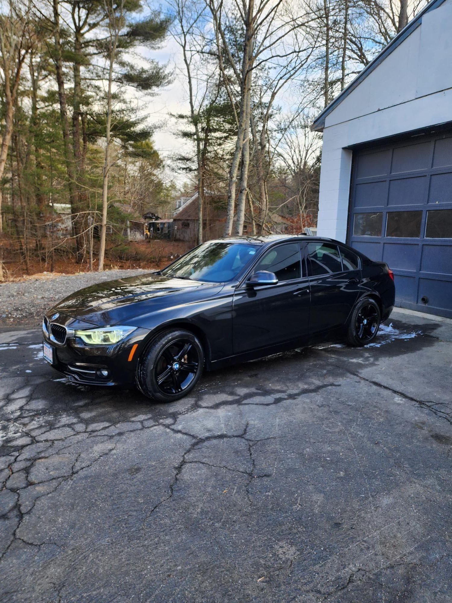 Black BMW sedan parked on a wet driveway, next to a garage on a sunny day.
