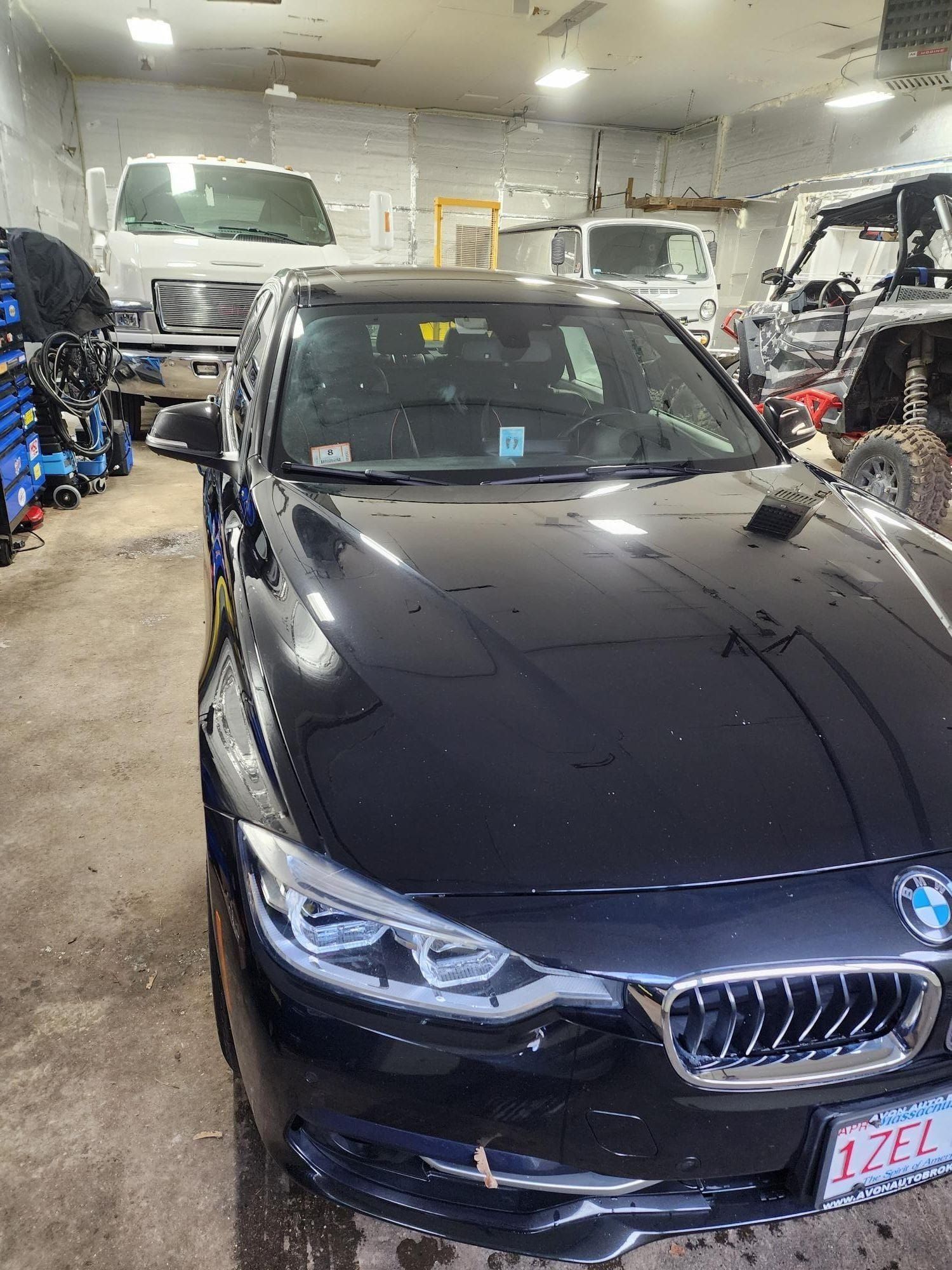 Black BMW car inside a garage, with a white truck and various tools and vehicles in the background.
