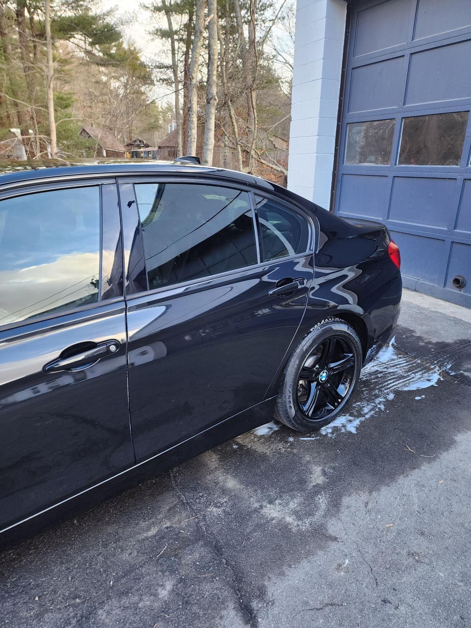 Black sedan parked outside a garage, reflecting sky.