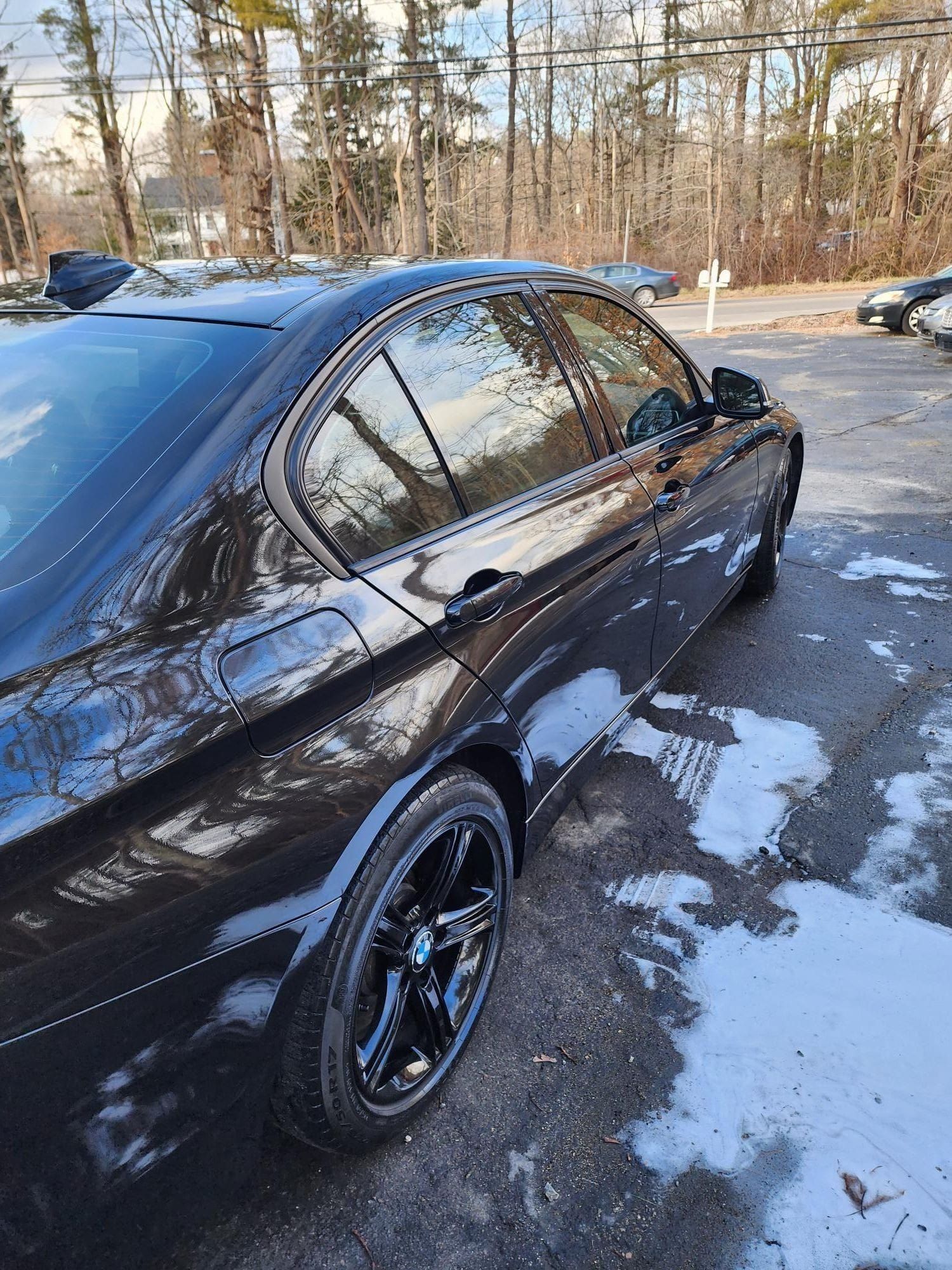 Black car parked on snowy asphalt, trees in the background.