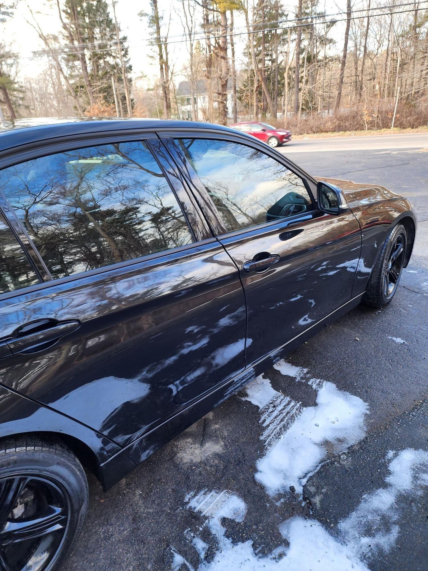 Black car parked on snowy asphalt, trees in the background.