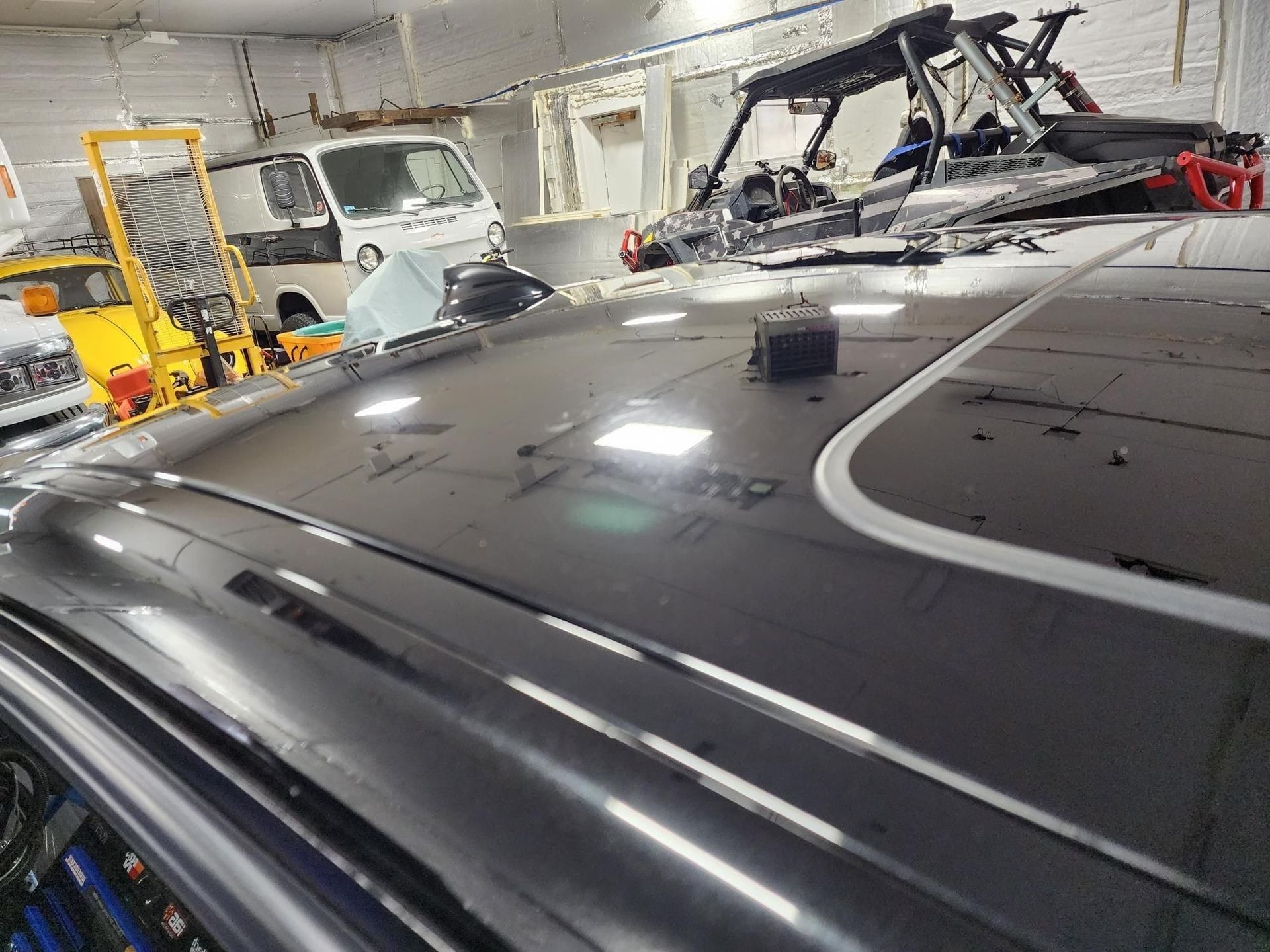 Black car roof in auto repair shop with damaged sunroof and other vehicles in the background.