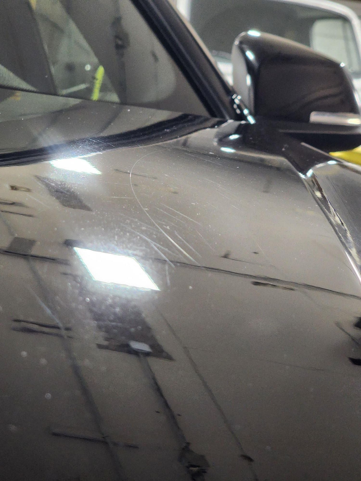 Black car hood with light scratches reflecting bright overhead lights.