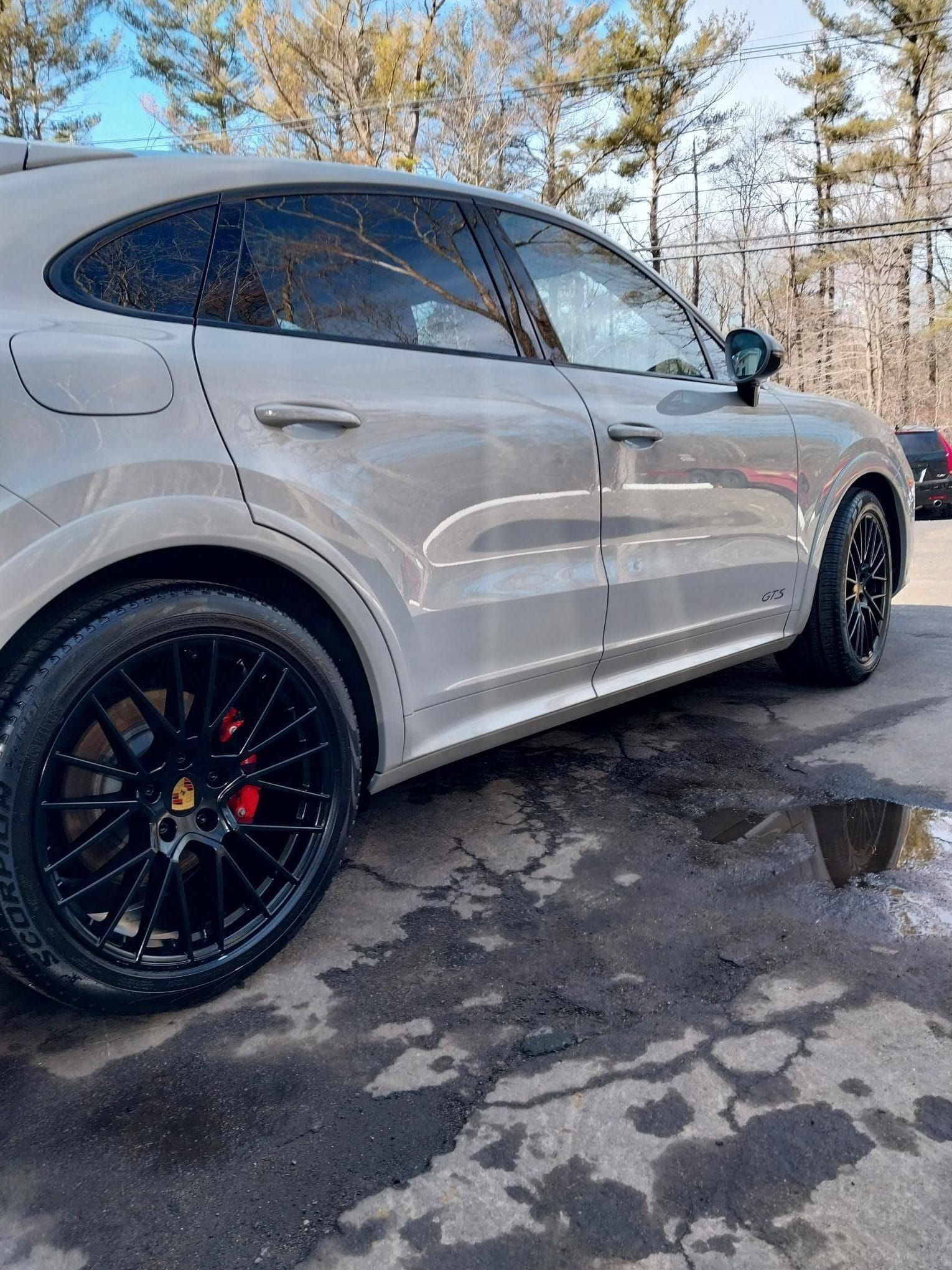Gray Porsche SUV with black wheels and red brake calipers parked on wet pavement.