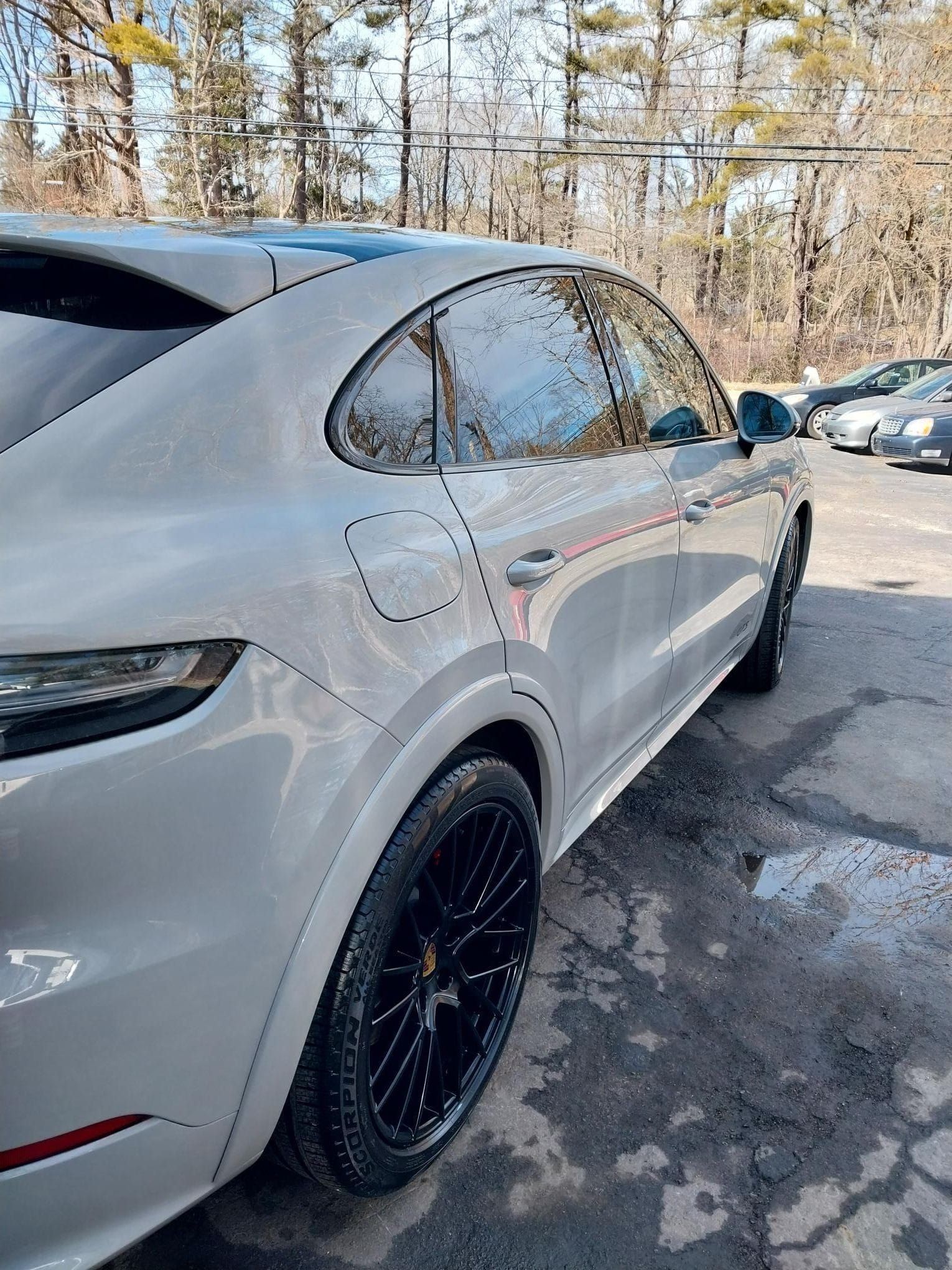 A light gray Porsche SUV with black wheels parked outdoors on a sunny day.
