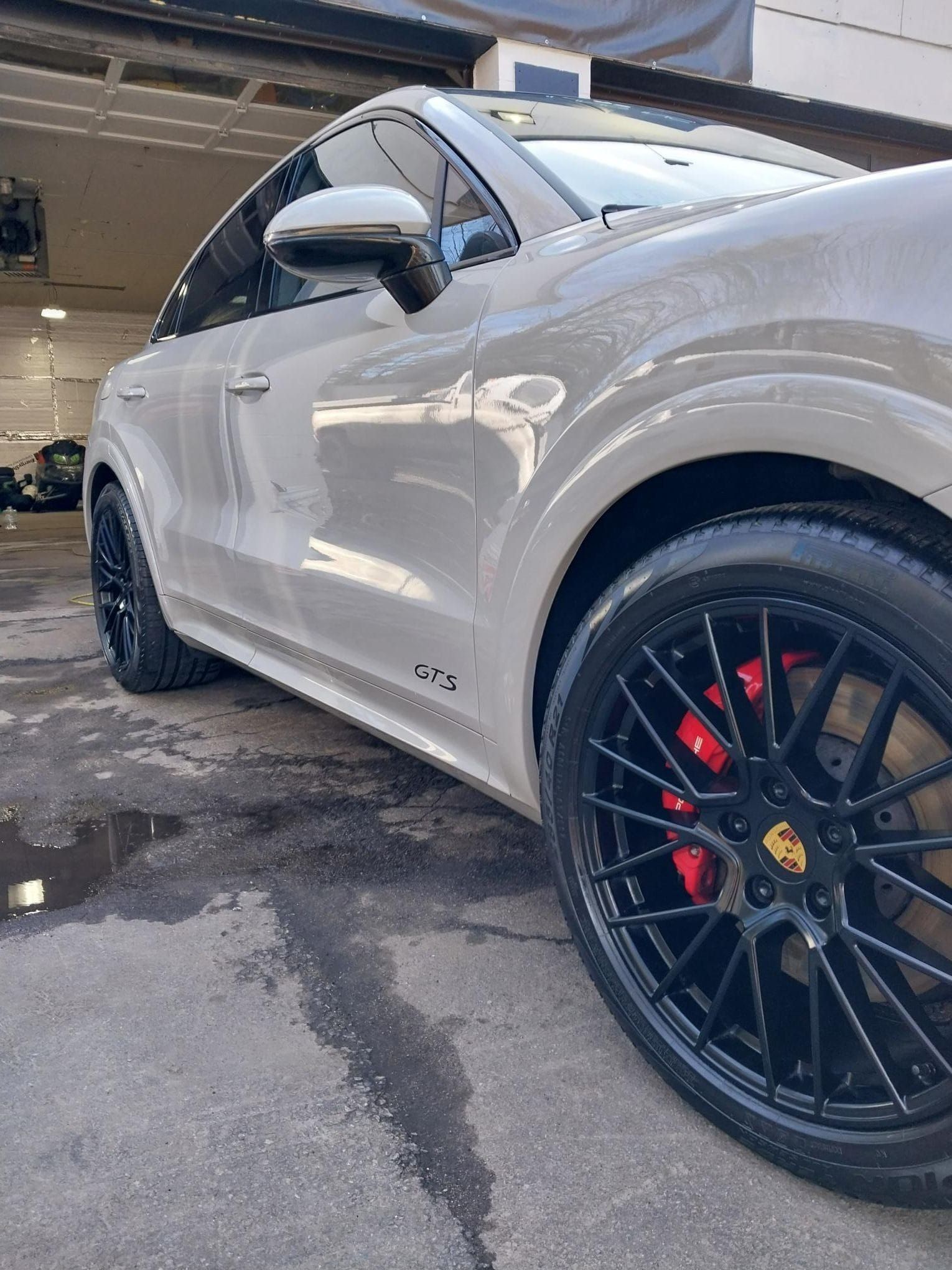 Gray Porsche SUV with black rims and red brake calipers, parked on wet pavement.