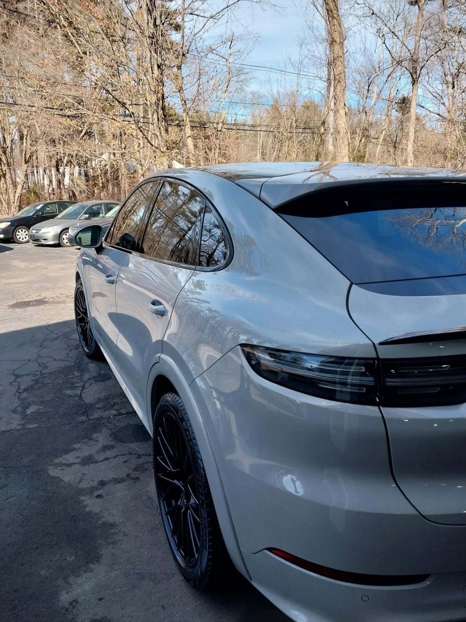 Gray Porsche SUV with black rims and red brake calipers, parked on wet pavement.