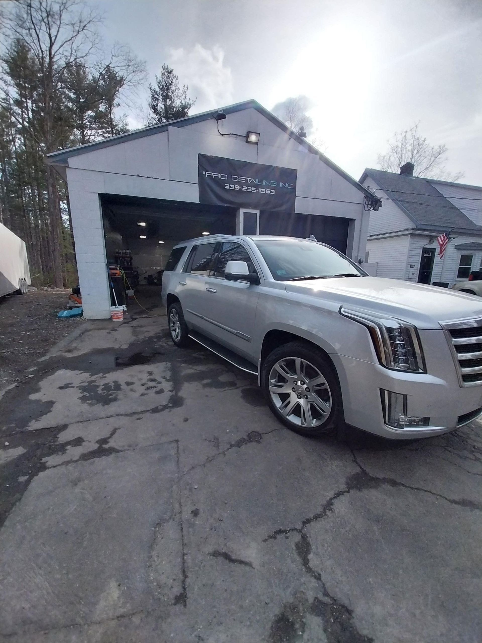 Silver Cadillac SUV parked in front of a garage with open door, outdoors on a cloudy day.