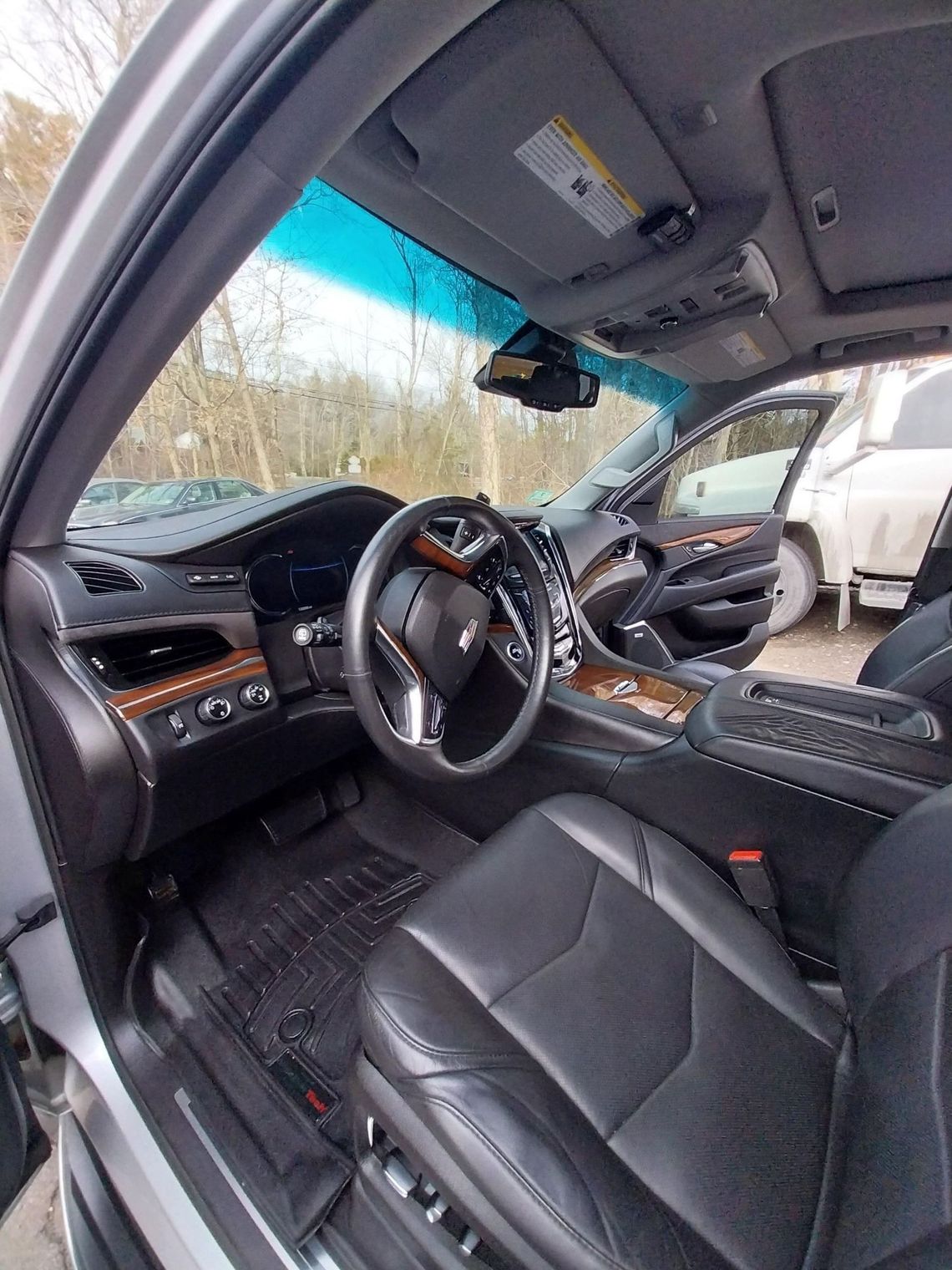 Interior view of a Cadillac Escalade, featuring black leather seats, wood trim, and the steering wheel.