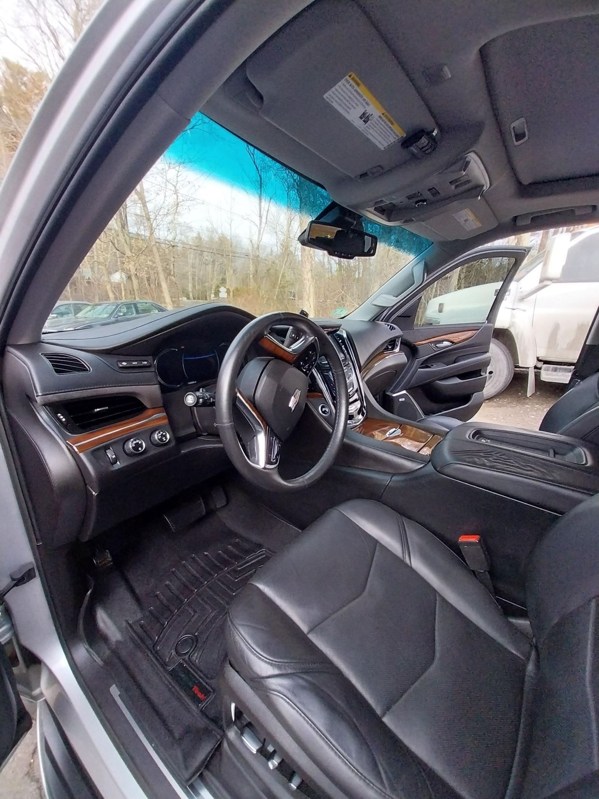 Interior view of a Cadillac SUV, black leather seats, wood trim, and a steering wheel.