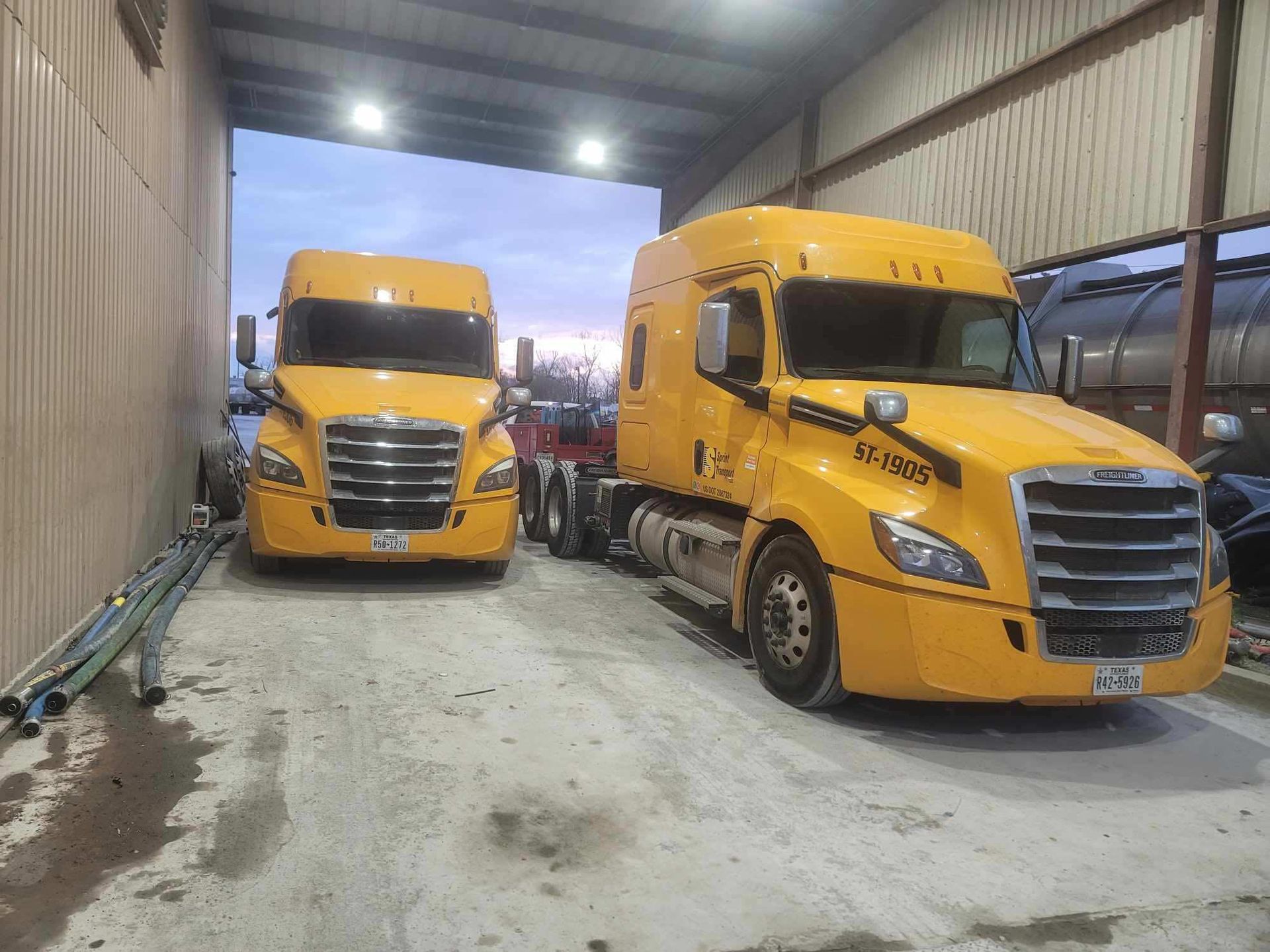 Two yellow semi trucks are parked next to each other in a garage.