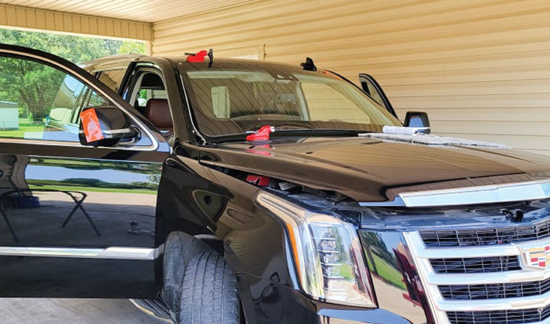 A black cadillac escalade is parked in a garage with its doors open.