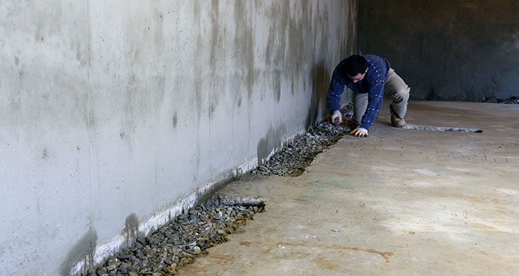 A man is working on a concrete wall in a basement.