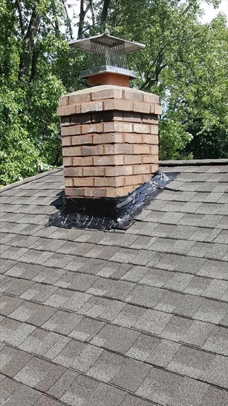 A brick chimney on top of a roof with trees in the background.
