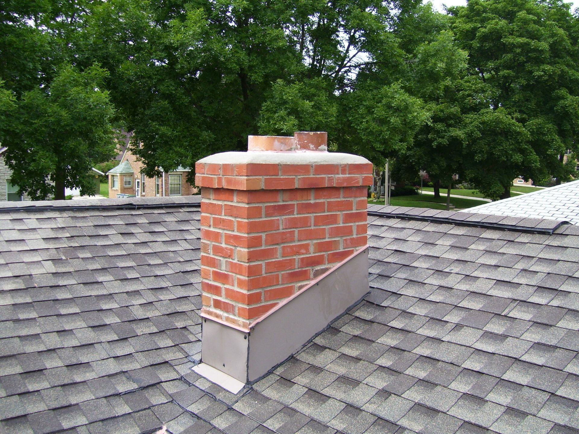 A neat-looking brick chimney on top of a roof with trees in the background