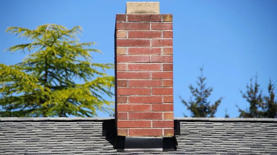 A brick chimney on top of a roof with trees in the background.