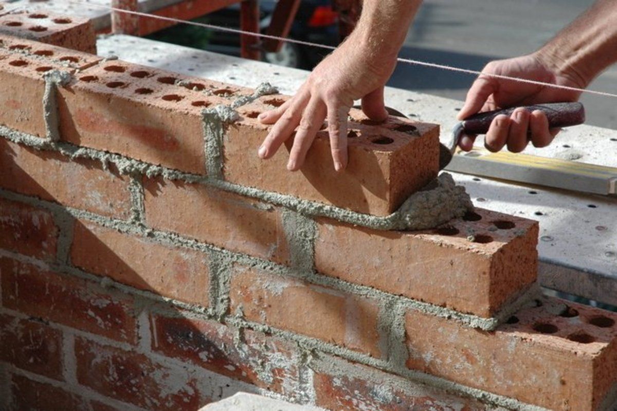 A person is laying bricks on a wall with a trowel.