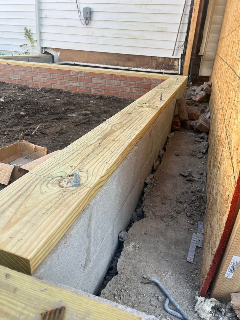 A wooden plank is sitting on top of a concrete wall next to a house.