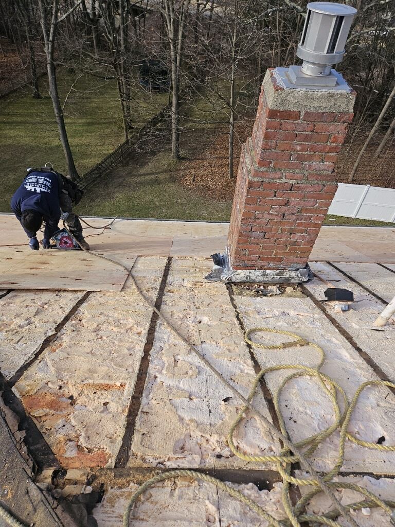 A man is working on a roof with a brick chimney.