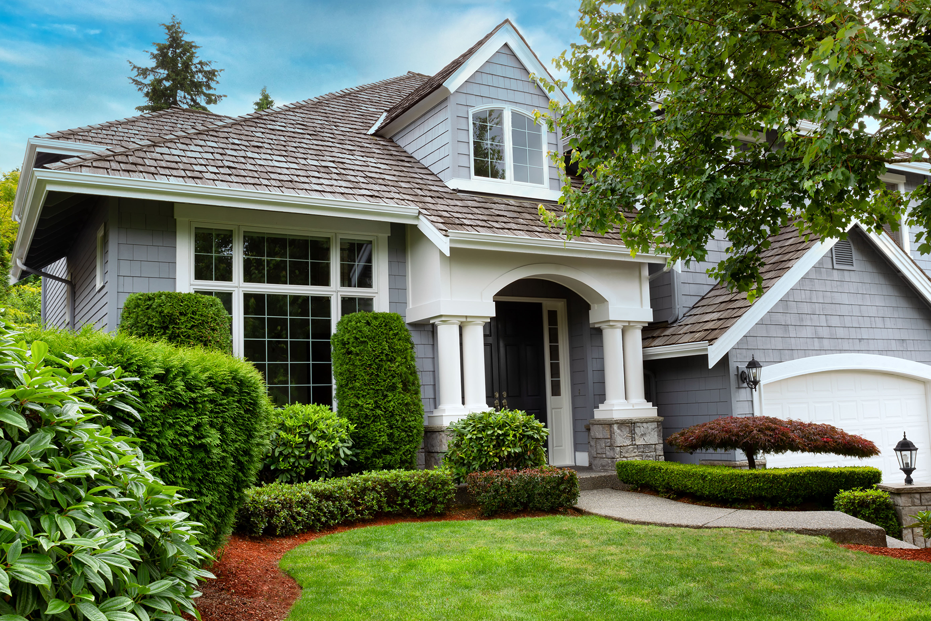 A gray and white house with a large lawn in front of it.