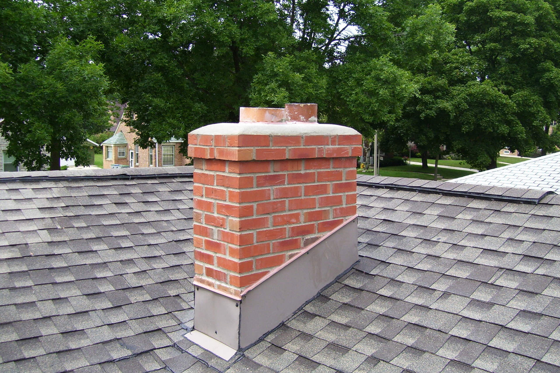 A brick chimney on top of a roof with trees in the background