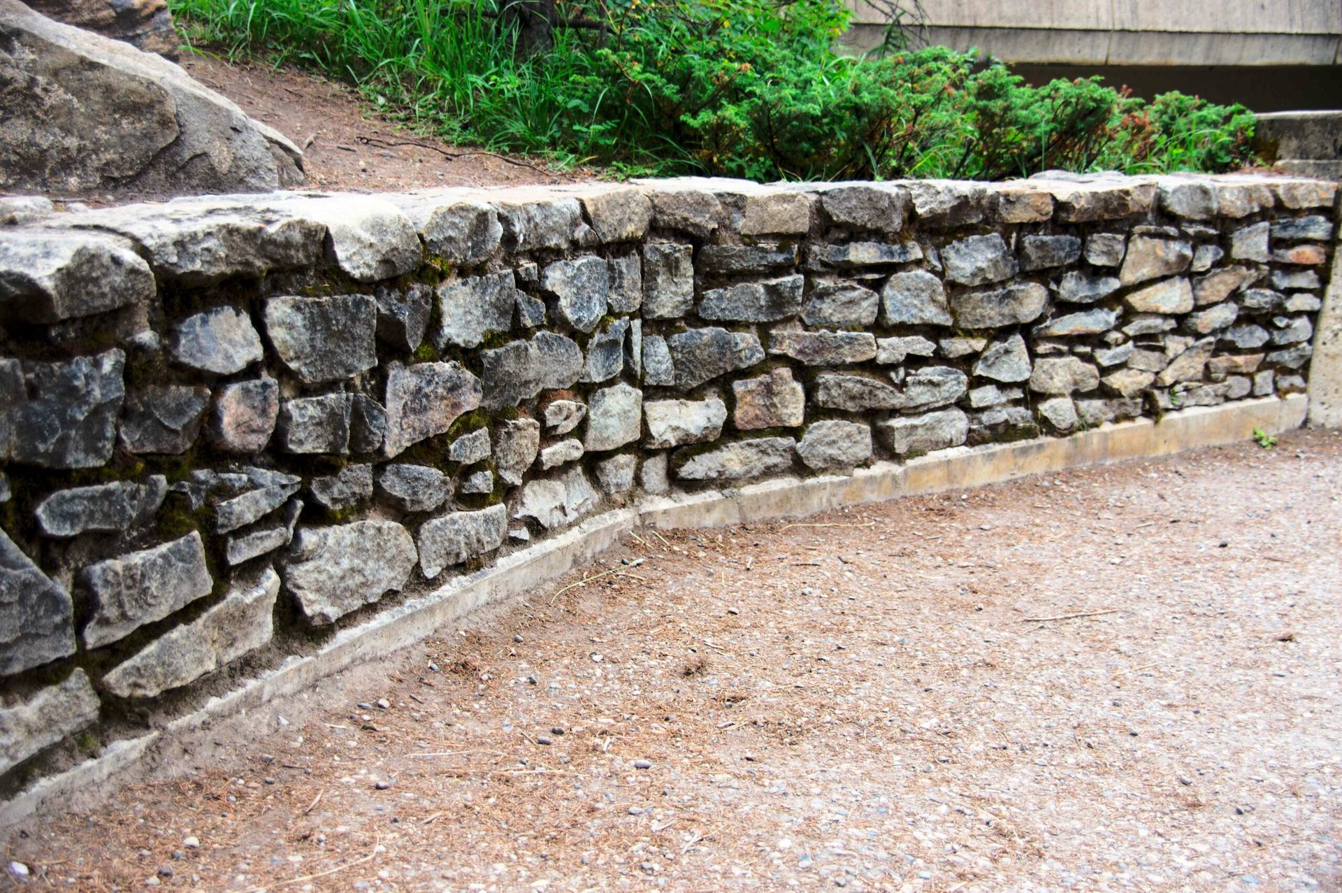 A stone wall is surrounded by gravel and trees