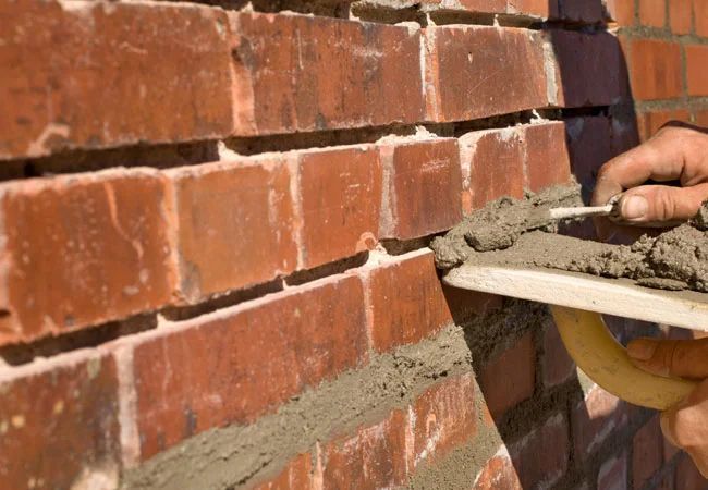 A person is laying bricks on a brick wall with a trowel.