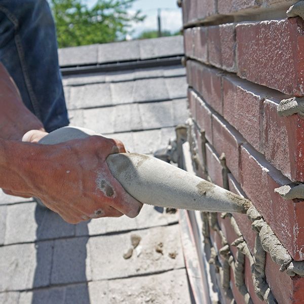 A person is working on a brick wall with a trowel