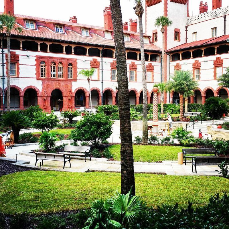 Courtyard of the Ponce de Leon Hotel in St. Augustine, Florida. Red brick facade, lush green lawn, palm trees.