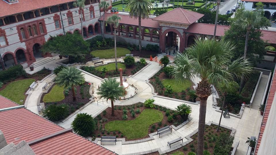 Courtyard with walkways, green lawns, palm trees, and red-tiled roof buildings in St. Augustine, Florida.
